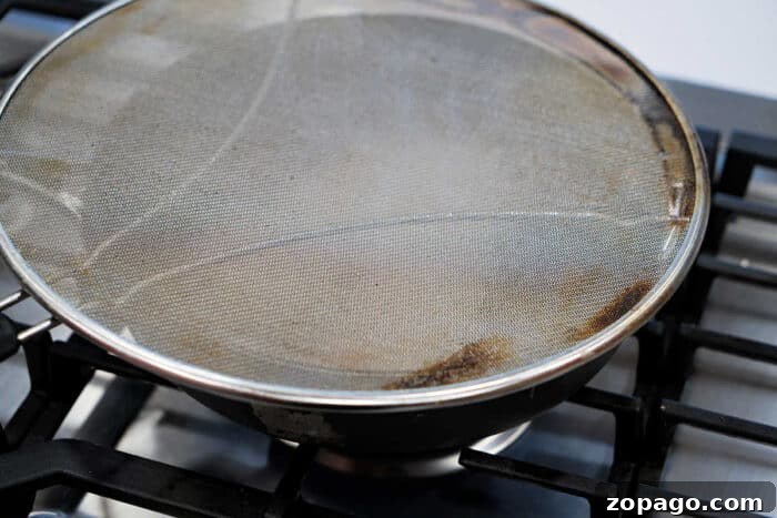 Crispy Fried Tilapia with Lemon and Herbs 9 A frying pan on a stove, covered with a metal mesh splatter screen, is perfect for preparing your favorite fried tilapia recipe.