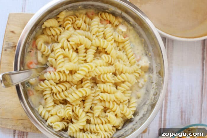 Cheesy Ritz Chicken Casserole with Crunchy Cracker Topping 5 A metal bowl with rotini pasta mixed in a creamy sauce, reminiscent of the comforting flavors found in a Ritz Chicken Casserole, with a spoon inside the bowl.